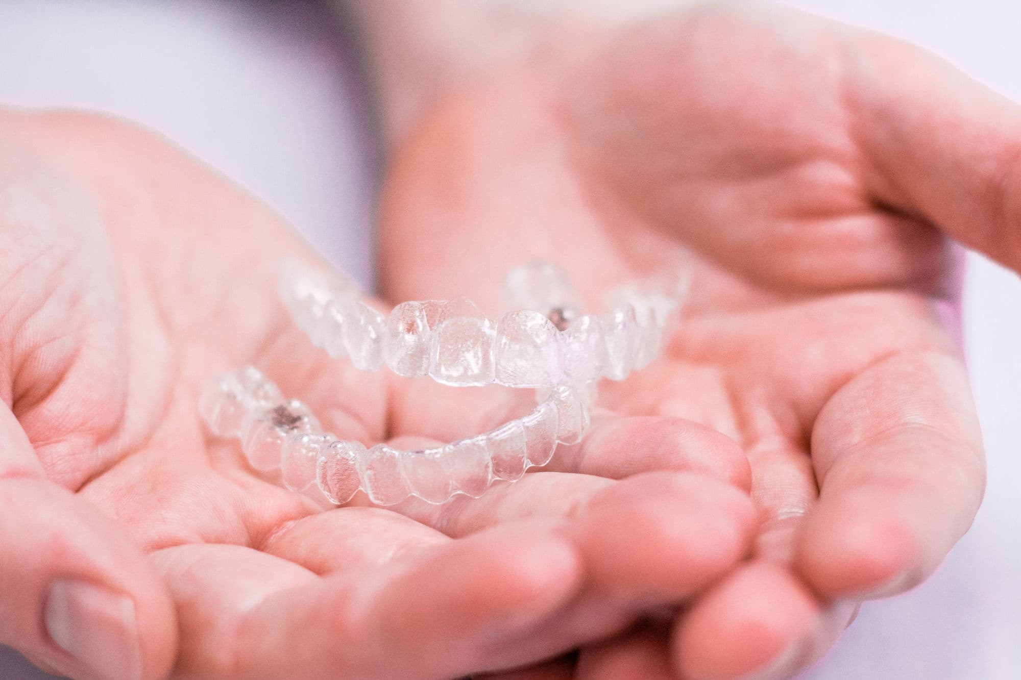 Clear aligners held in hands, showcasing transparent orthodontic trays for teeth alignment, related to Johnston Family Orthodontics in Crosby, Texas.